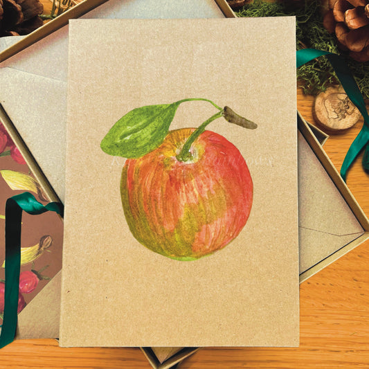 Cox apple illustrated in watercolour attached to Manila recycled blank greetings card laying on a box next time accompanying woodland walk illustrated inlay envelope