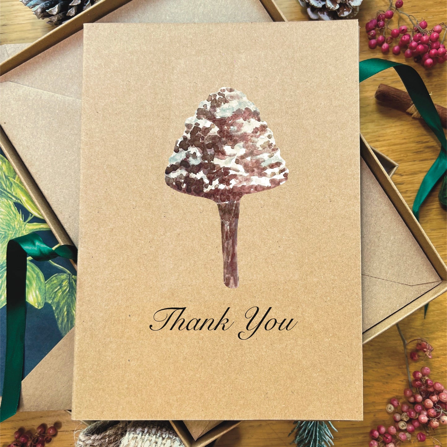 Brown manila recycled greetings card featuring a watercolour painted snow topped Mottlegill mushroom. Text underneath the mushroom says Thank You printed in italic black script.