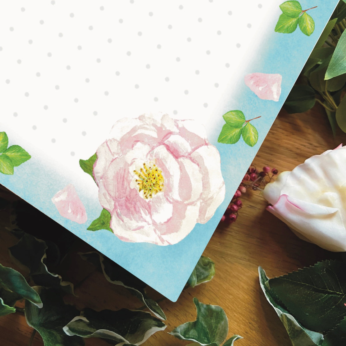 Close up corner of light pink rose illustrated dotted notepad with sky blue border decorated with light pink petals and leaves