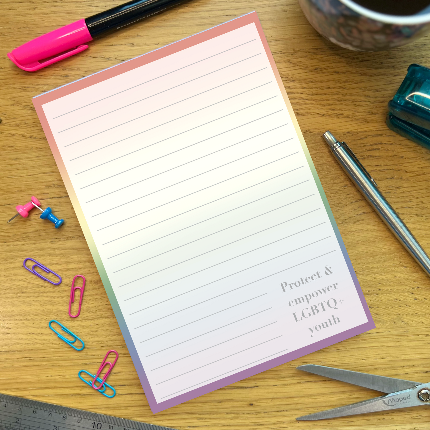 Rainbow pride notepad with quote Protect and empower LGBTQ youth, on a wooden desk with stationery