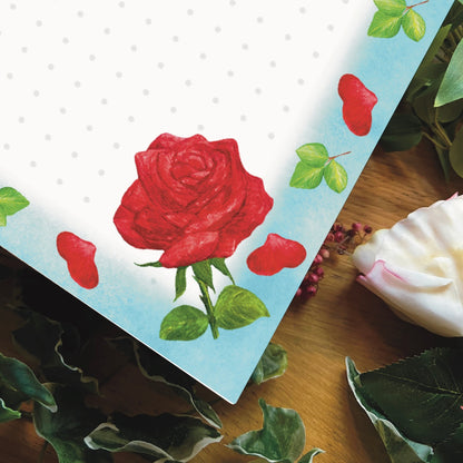 Close up corner of red rose illustrated blank notepad with sky blue border decorated with red rose petals and leaves