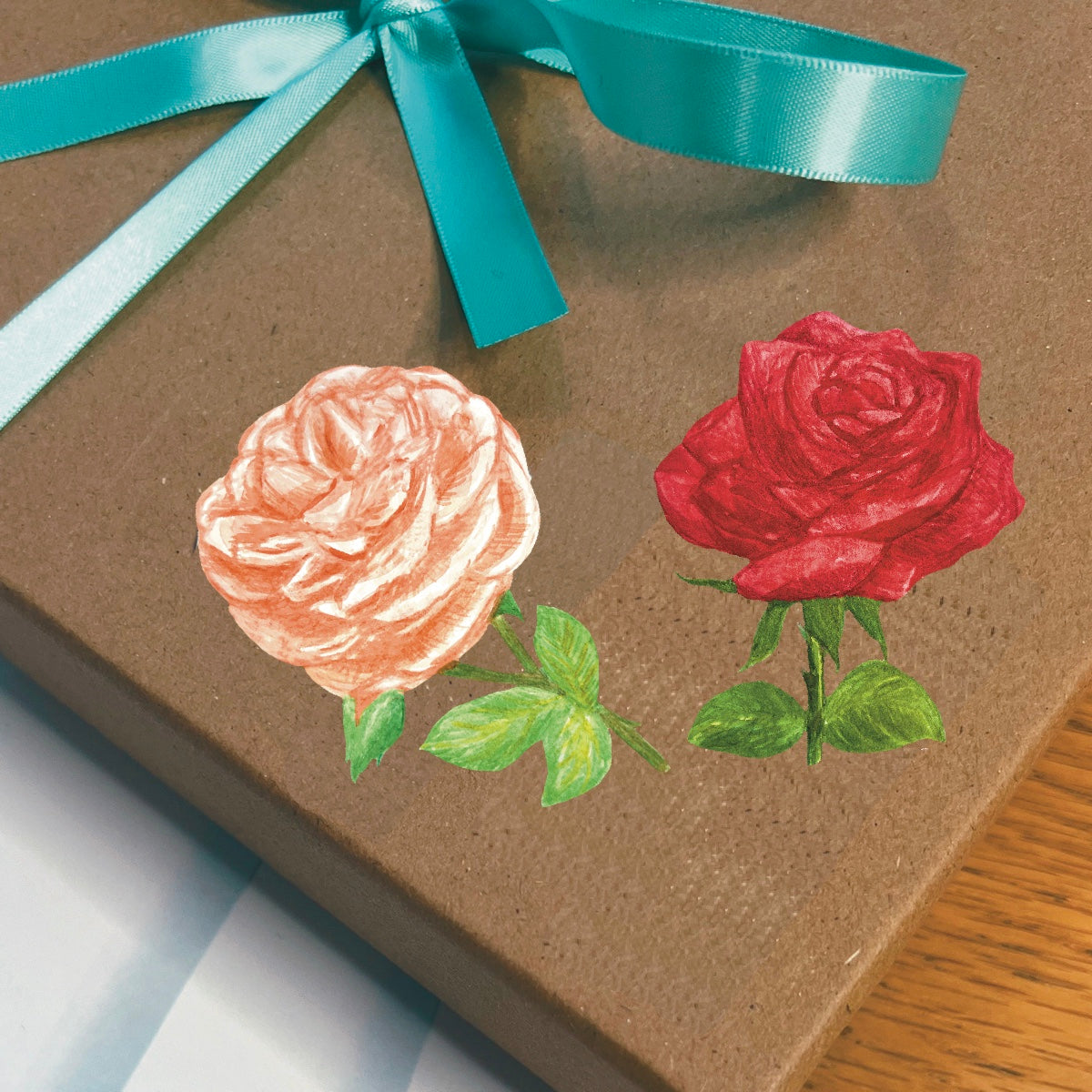 A blossoming peach and red rose set of die cut stickers with and easier to peel edge on a gift box wrapped with a blue ribbon