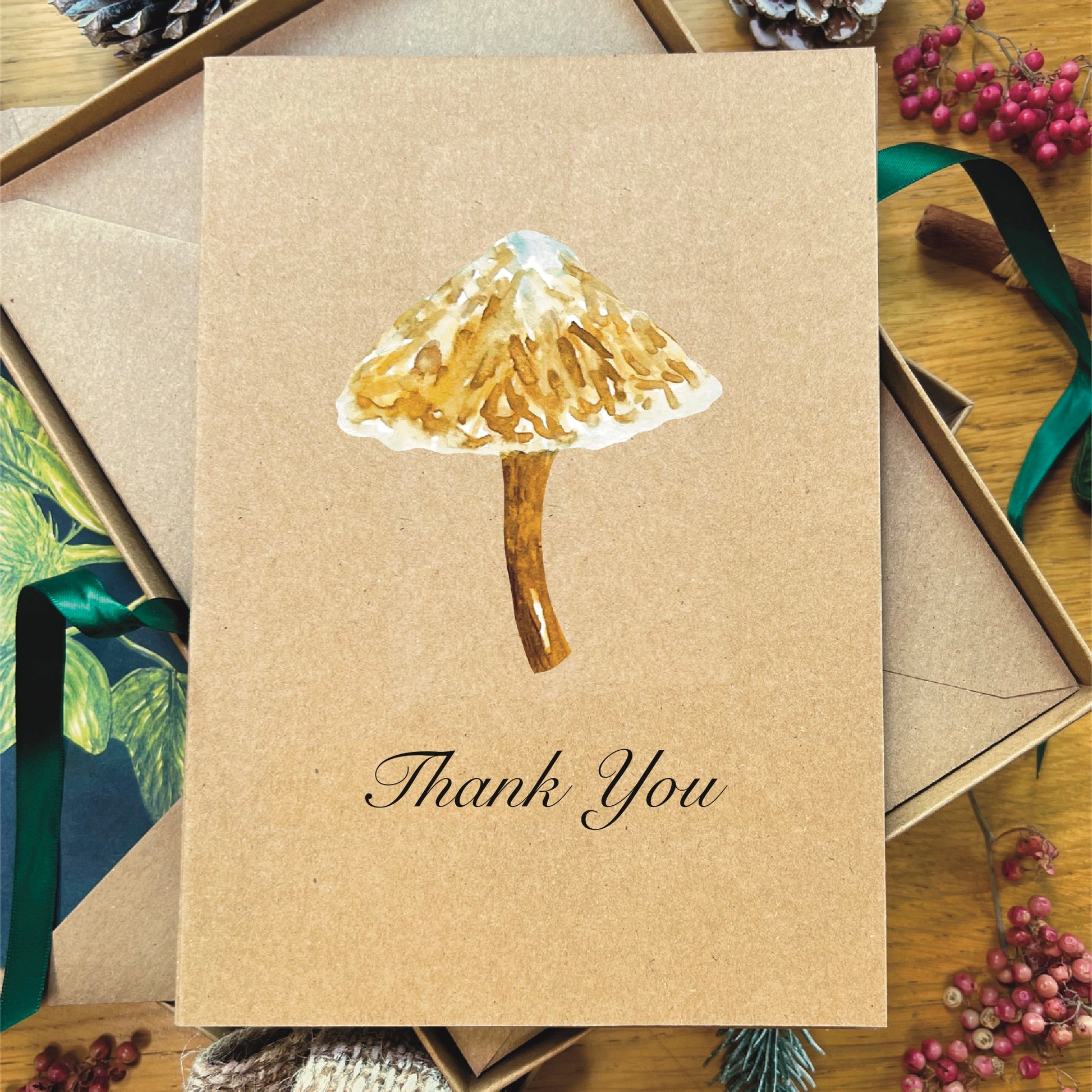 Brown manila recycled greetings card featuring a watercolour painted snow topped Slimy Waxcap mushroom. Text underneath the mushroom says Thank You printed in italic black script.
