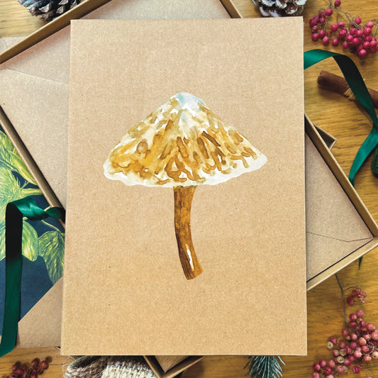 Snow topped slimy Waxcap mushroom illustrated in watercolour attached to Manila recycled greetings card on a wooden desk