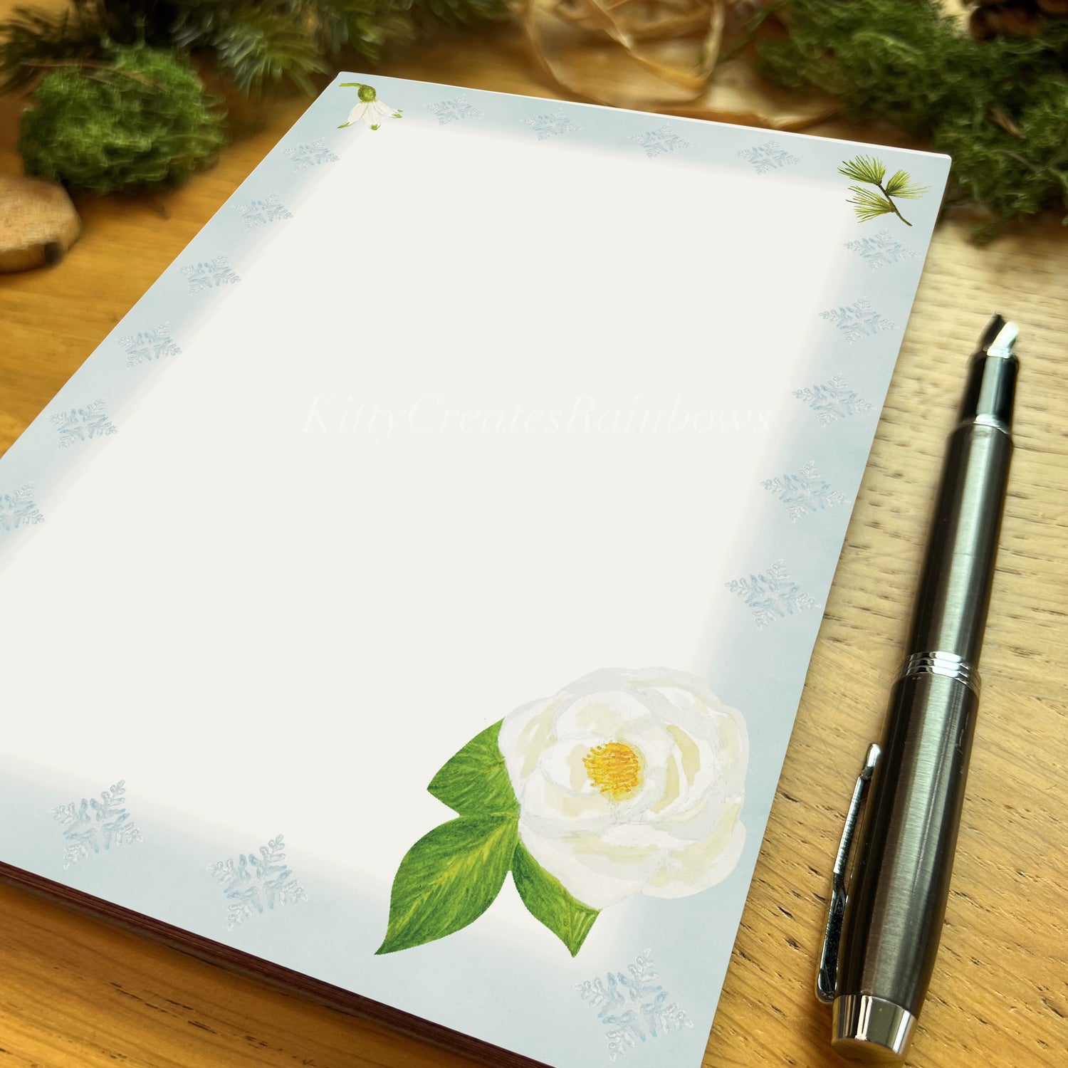 White rose illustrated notepad page with icy blue border on a wooden desk with a fountain pen