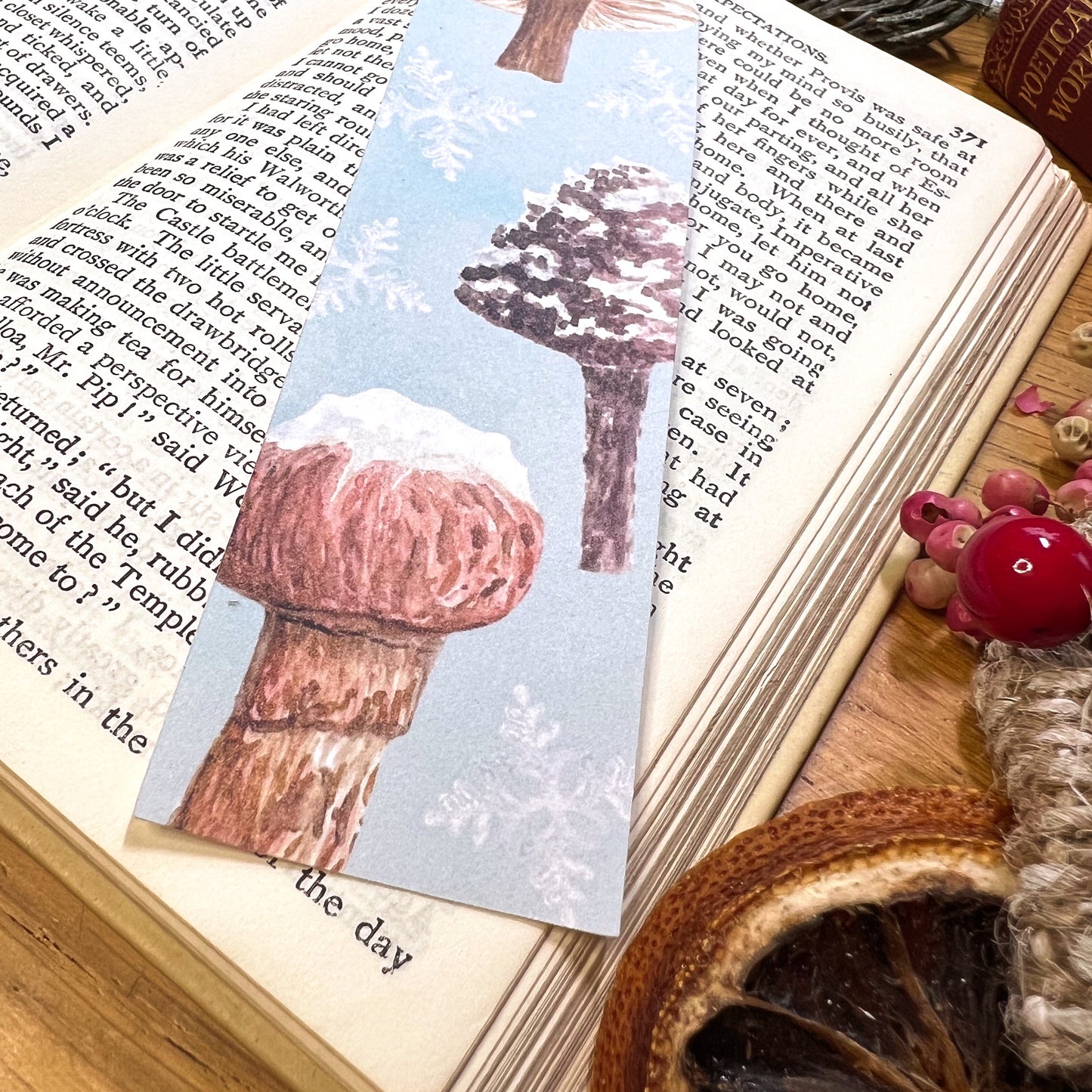 Close up of Winter wanderland snow topped mushroom illustrated bookmark, cut at the top to the shape of a snow topped milkcap mushroom