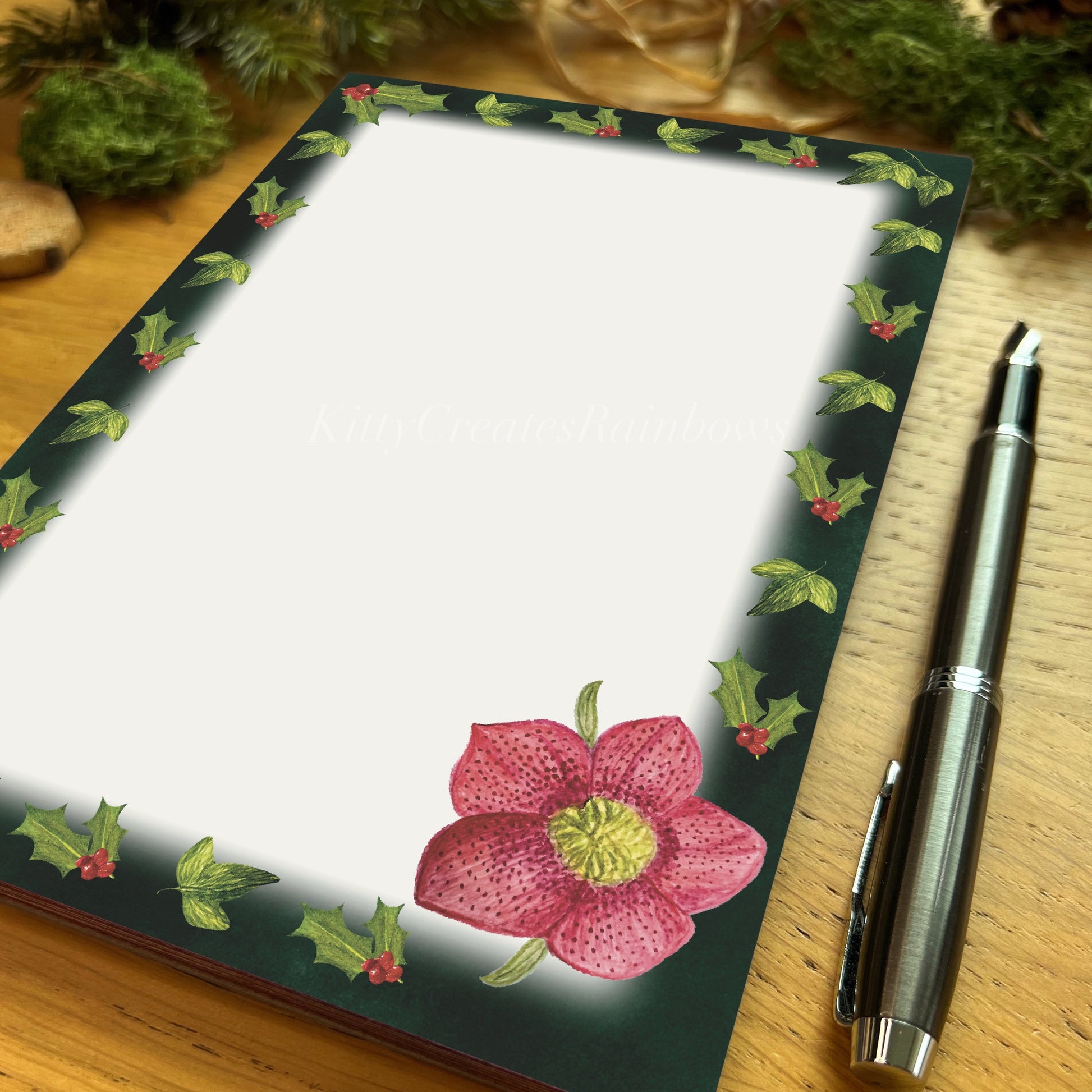 Hellebore illustrated notepad with dark evergreen border, on a wooden table with fountain pen