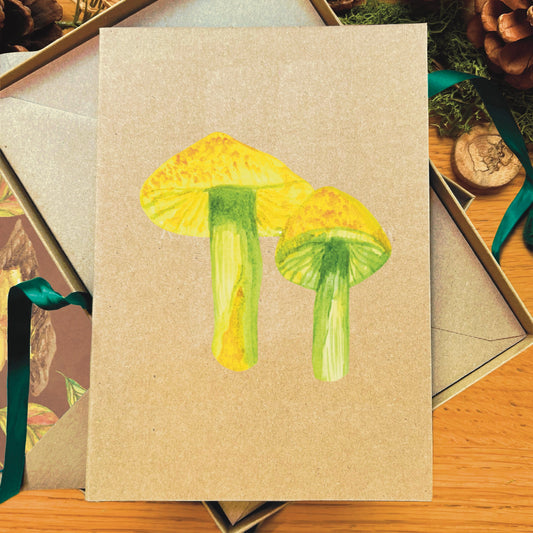 Green yellow parrot waxcap mushroom painted in watercolour attached to a natural recycled blank greetings card, laying in a box with an illustrated inlay envelope 