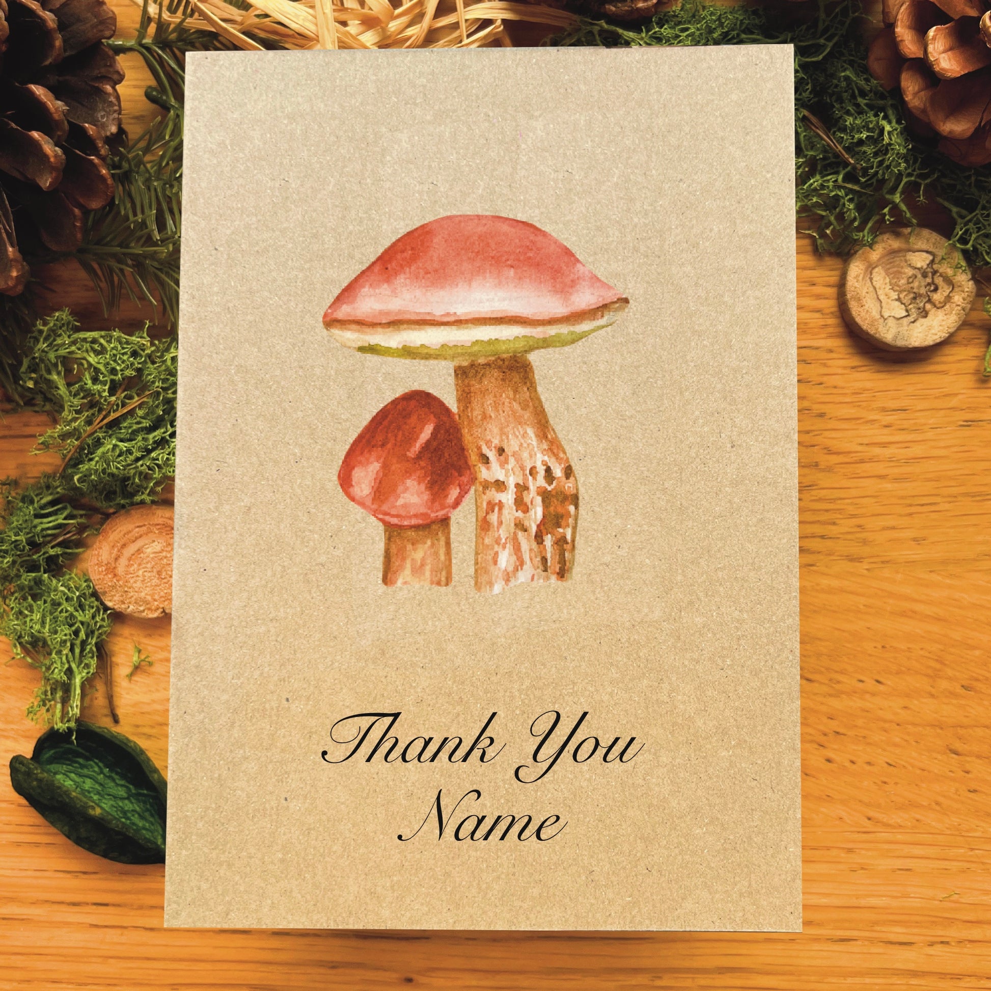 Penny bun mushroom illustrated in watercolour attached to Manila recycled greetings card on a wooden desk, with text script Thank You Name underneath the illustration