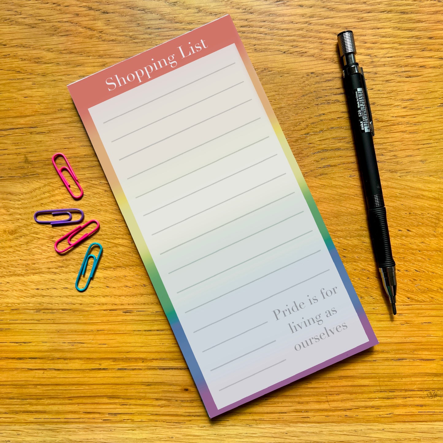 Rainbow shopping list with quote Pride is for living as ourselves, on a wooden desk