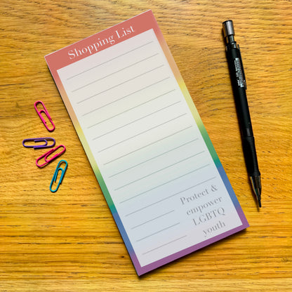 Rainbow shopping list pad with quote Protect and Empower LGBTQ youth sat on a wooden desk 