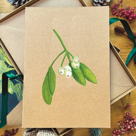 Snowdrop illustrated in watercolour attached to brown Manila recycled greetings card on a wooden desk