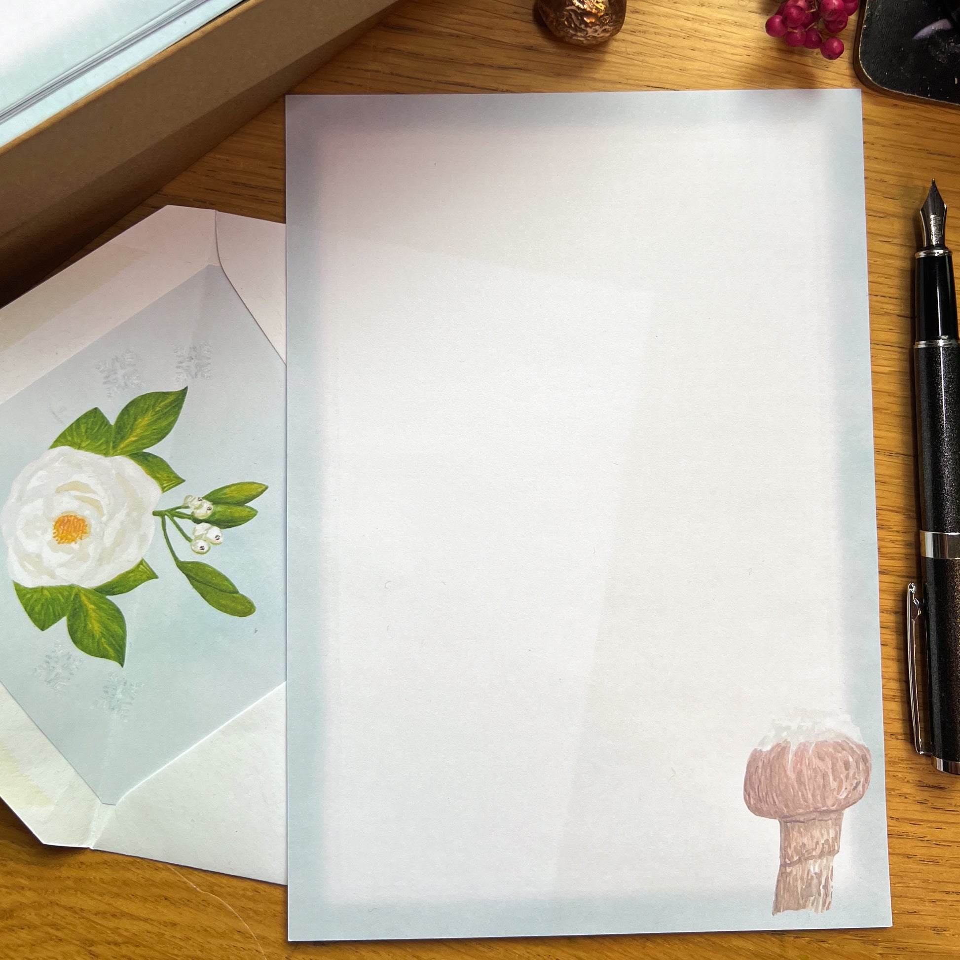 Snow topped honey fungus mushroom illustrated paper and white rose illustrated inlay in a white envelope, on a wooden desk