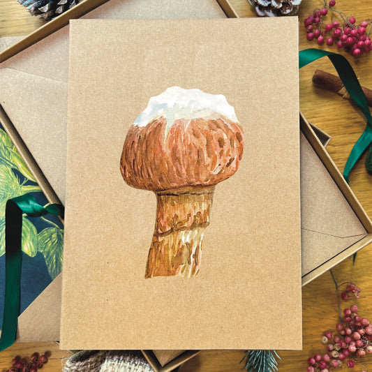 Snow topped honey fungus illustrated in watercolour attached to Manila recycled greetings card on a wooden desk