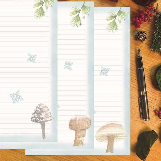 3 Winter wanderland illustrated papers featuring a snow topped mushroom with an ice blue border and snowflakes across the page, on a wooden desk