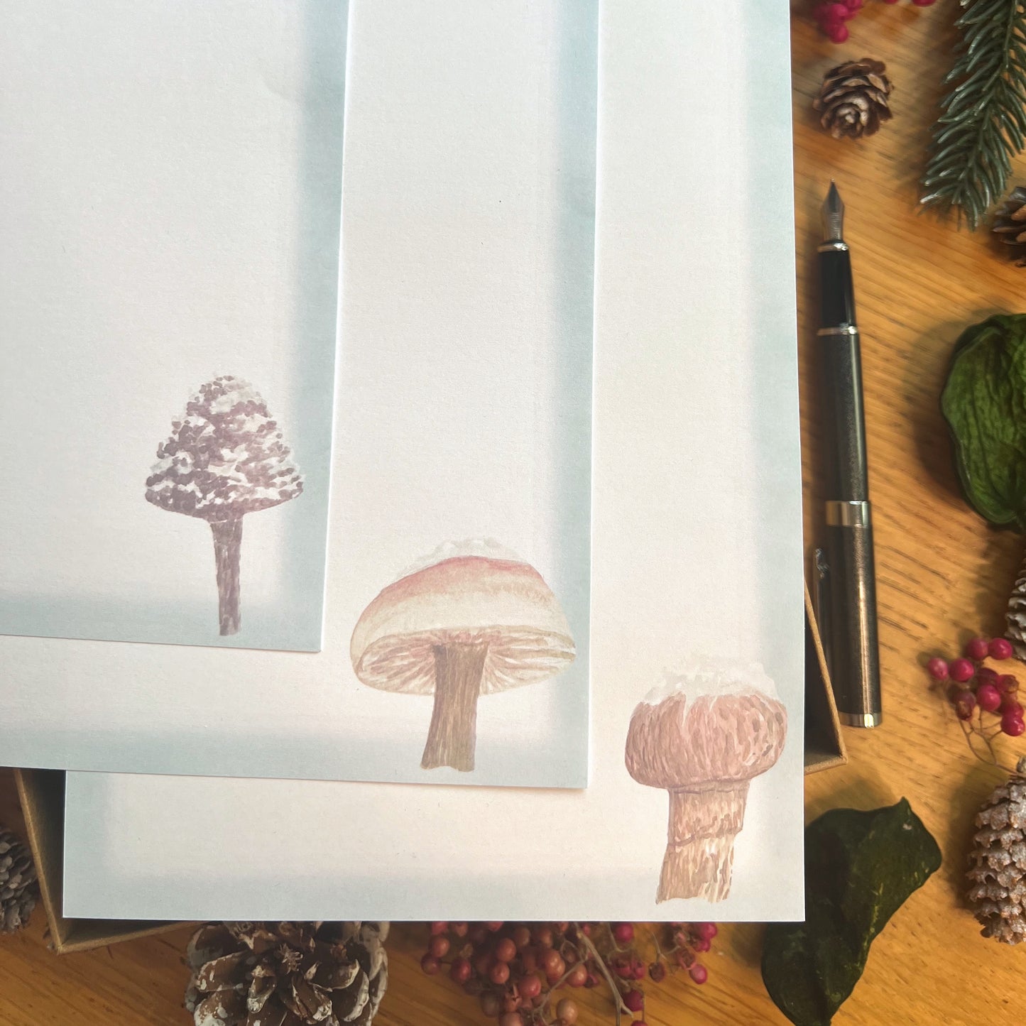 Winter wanderland illustrated paper set featuring snow topped mushrooms with an ice blue border, on a wooden desk
