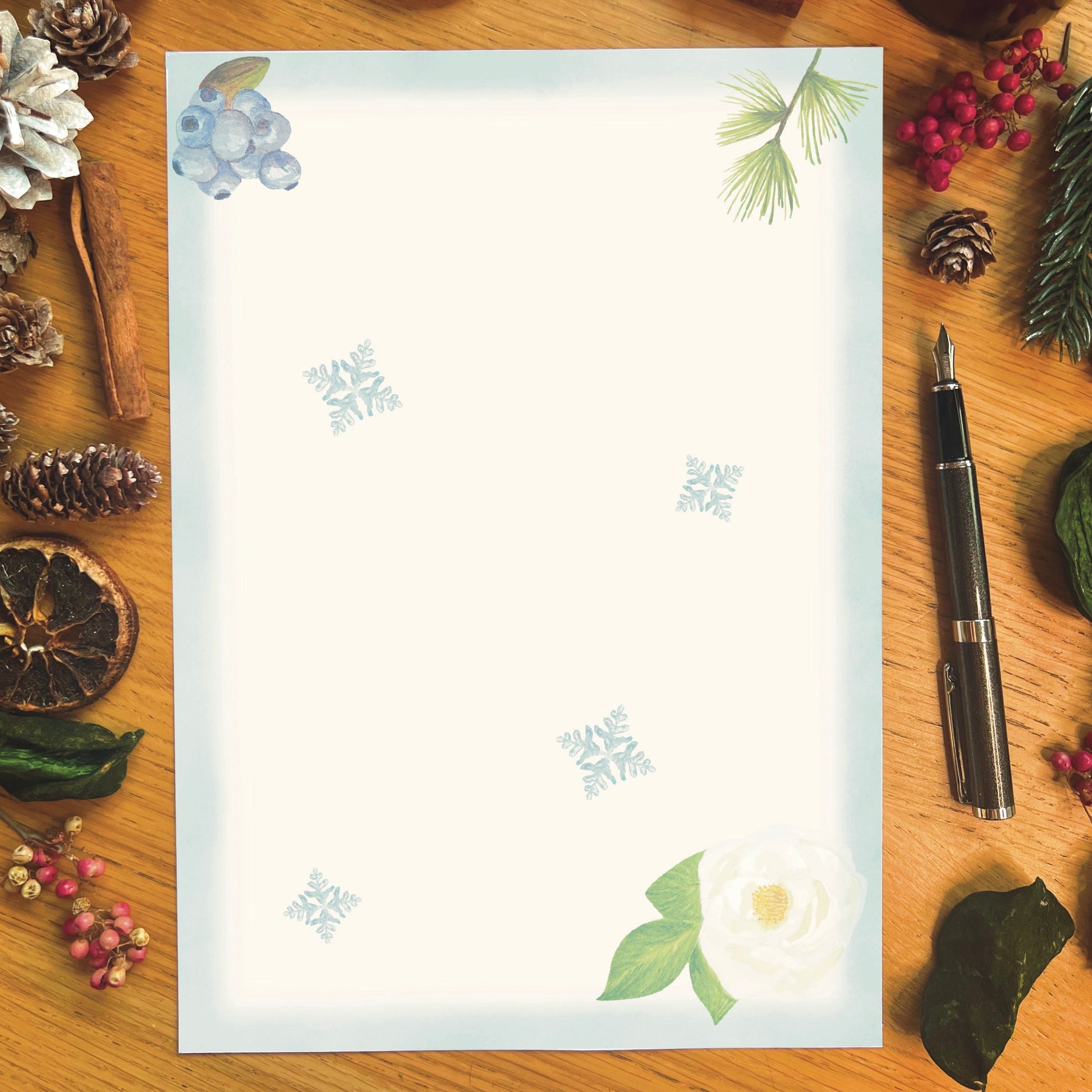 Winter wanderland illustrated paper featuring a white rose with an ice blue border and snowflakes across the page, on a wooden desk