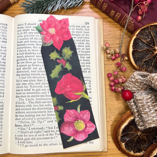 Winters bloom florals bookmark illustrated with hellebore, rose, holly and cut out at the top to the shape of a red poinsettia, resting on an open book