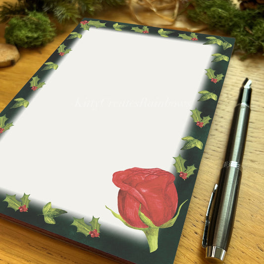 Red hybrid tea rose illustrated notepad with dark evergreen border, on a wooden table with fountain pen